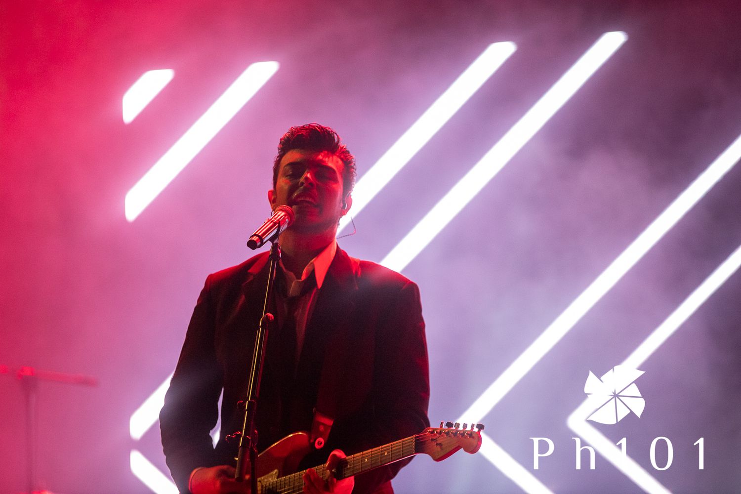 Concert stage lit with dramatic pink and white vertical light beams.