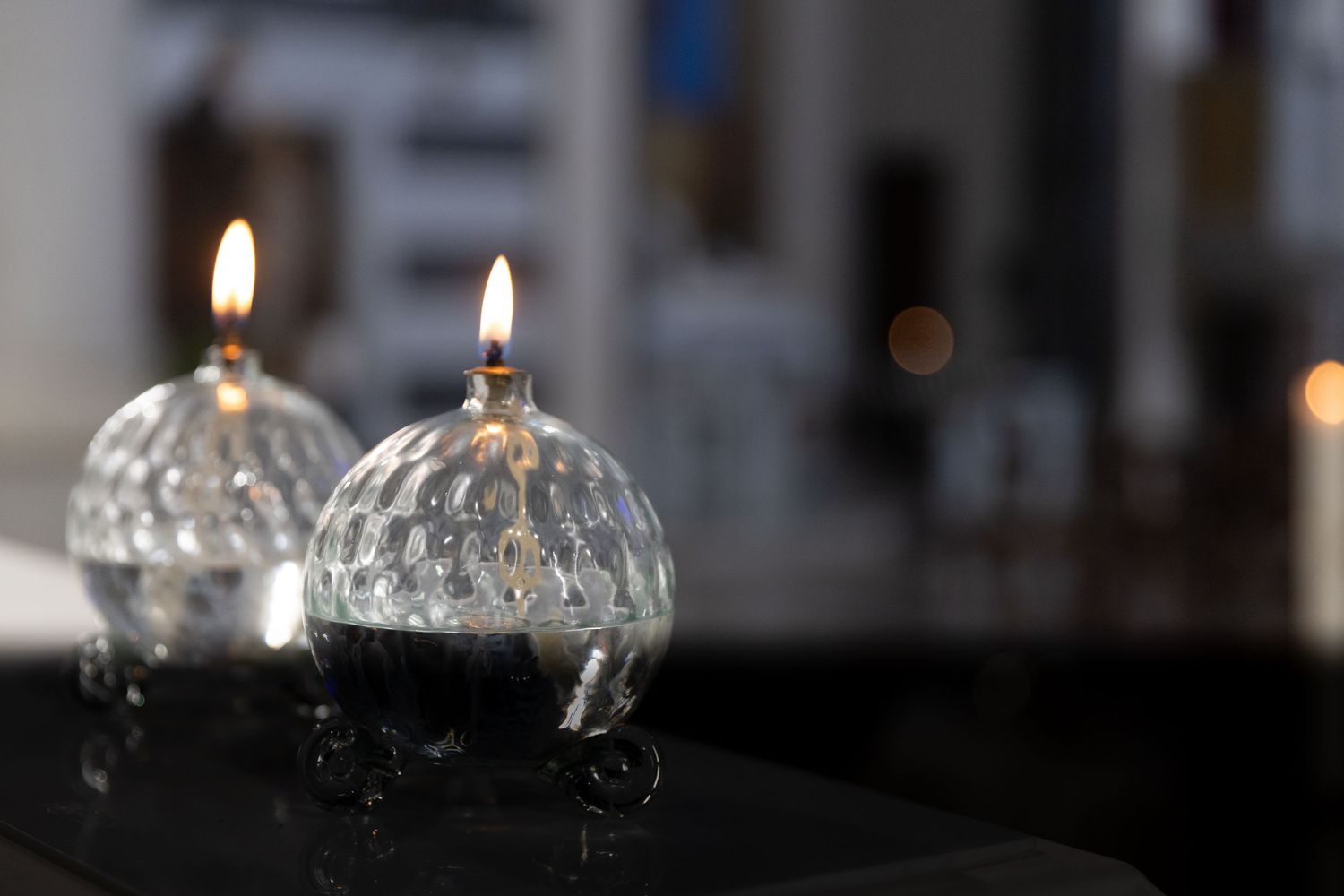 Glass candle holders reflect light while burning in a dimly lit environment.