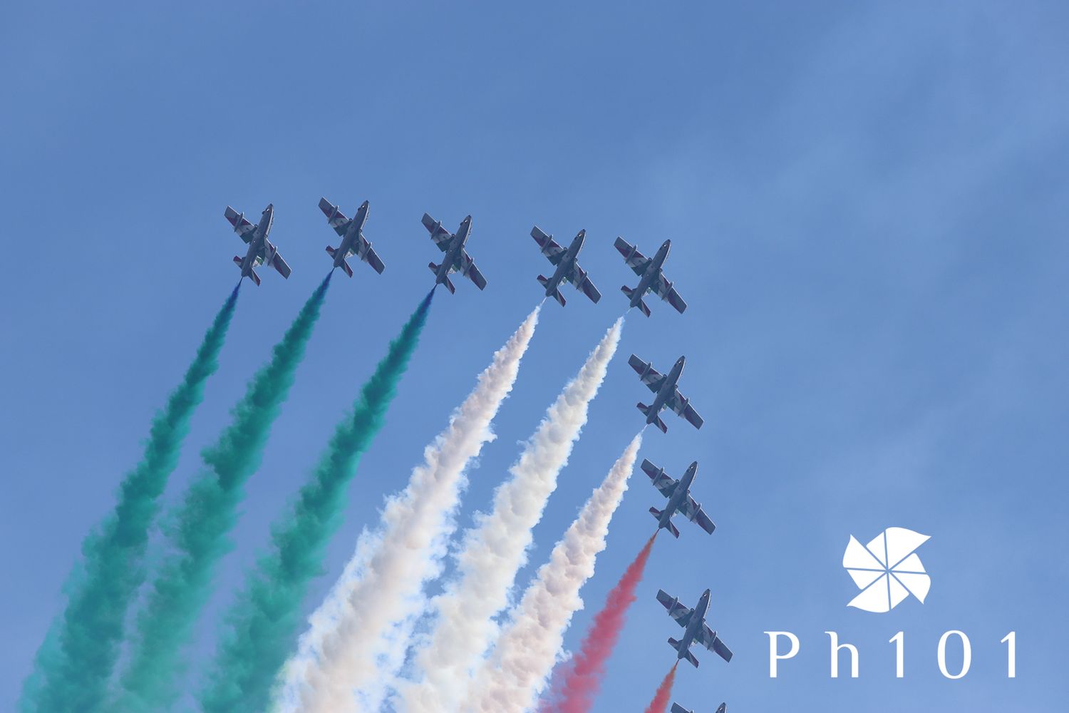 Formation of aircraft creating green, white and red smoke trails against blue sky.