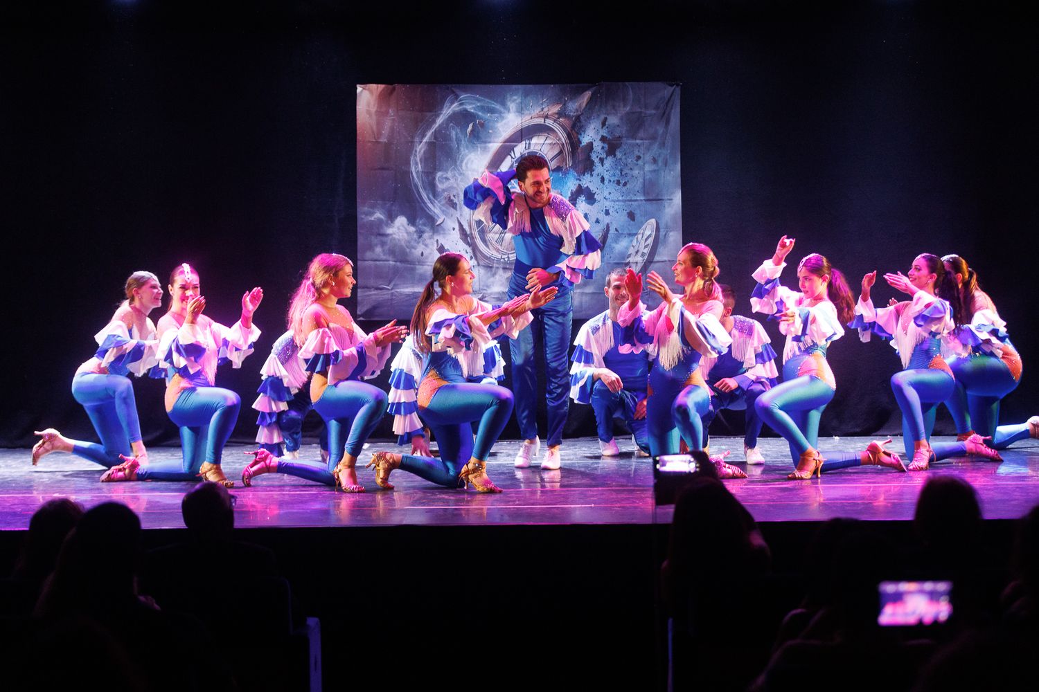 Dancers perform on stage in purple lighting during a theatrical production.