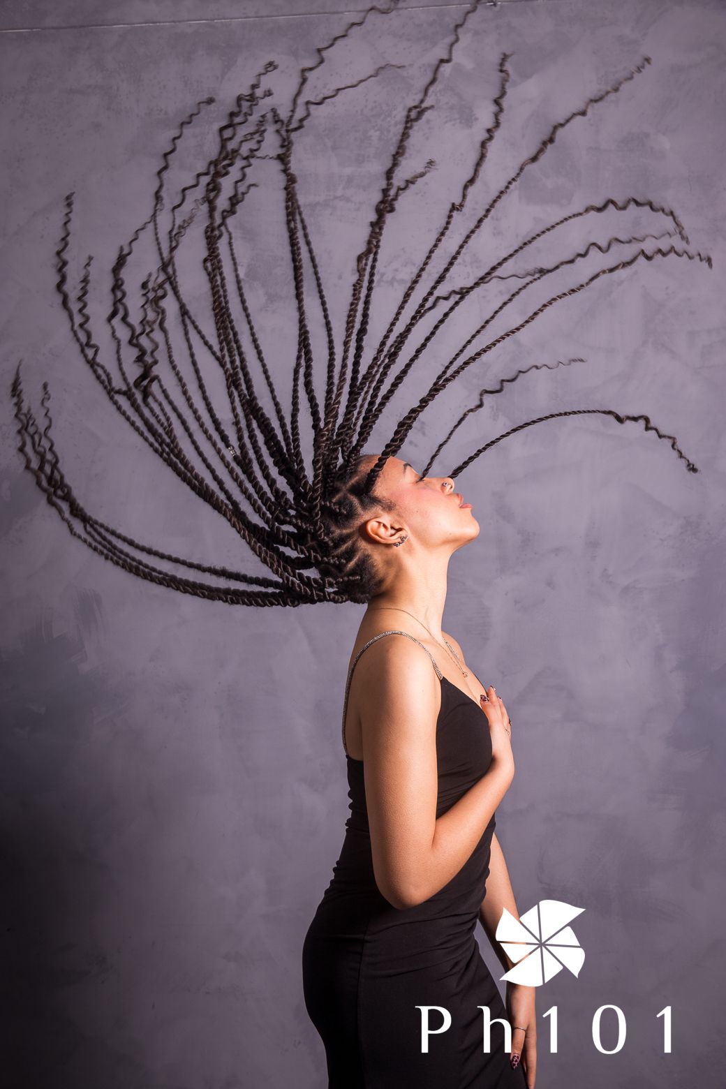 Dynamic portrait showing braided hair in motion against gray studio backdrop.