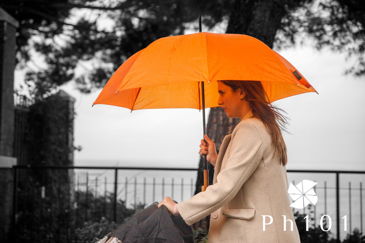 Orange umbrella stands out against moody black and white background creating dramatic contrast in rainy weather.