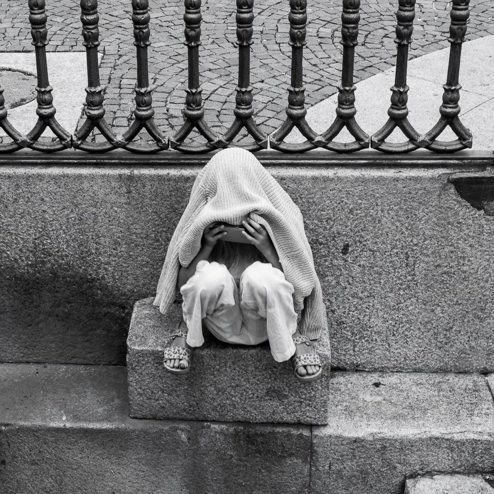 Black and white photo of person curled up against ornate metal railing.