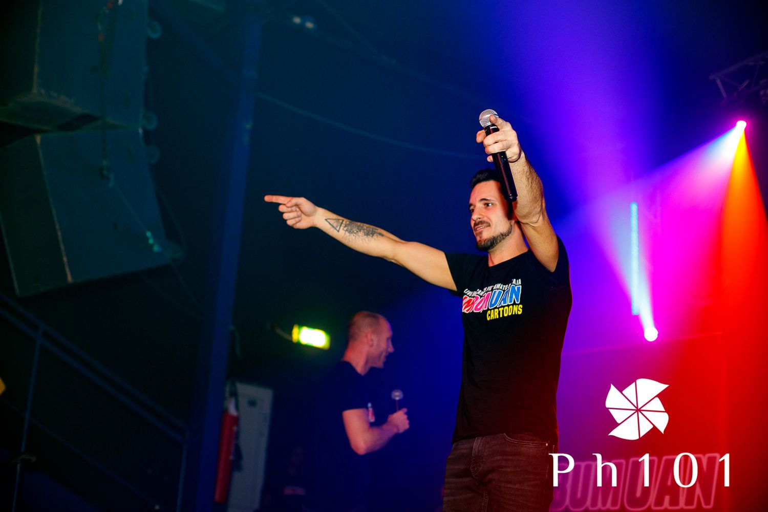 Performer on stage pointing during concert with colorful lighting effects.