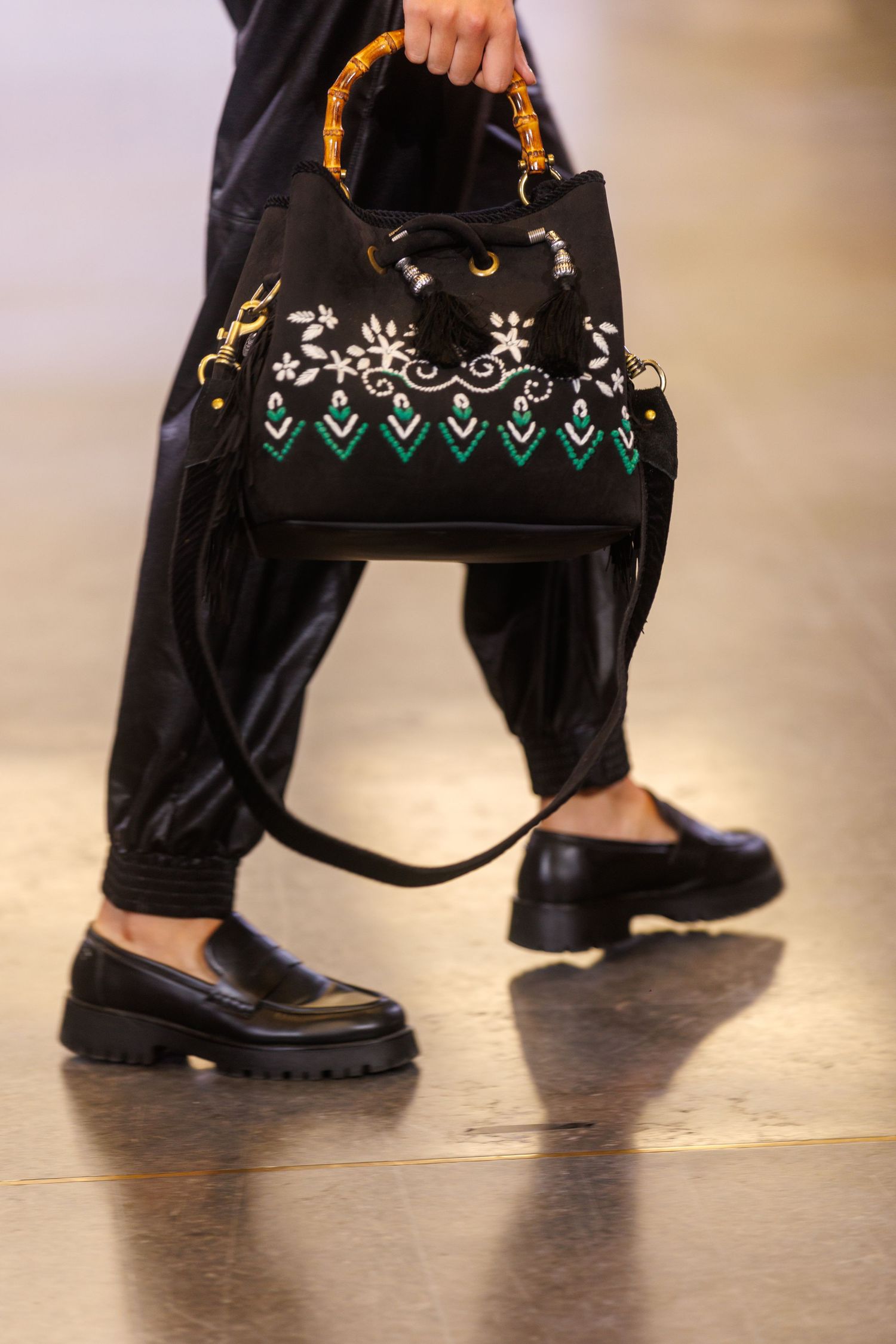 Close-up of black leather shoes and pants on a fashion runway with decorative embroidered details.