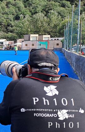 Photographer wearing black jacket taking photos at outdoor sports venue.