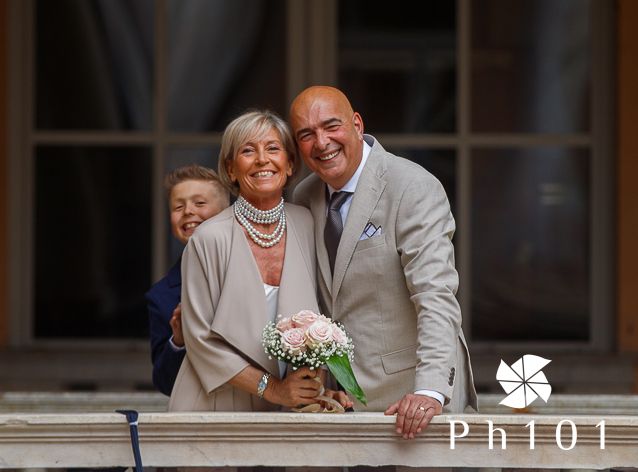 Happy mature couple posing together on a balcony with a small bouquet.