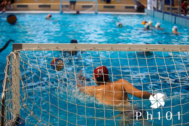 Water polo players competing in a pool with goal net visible.