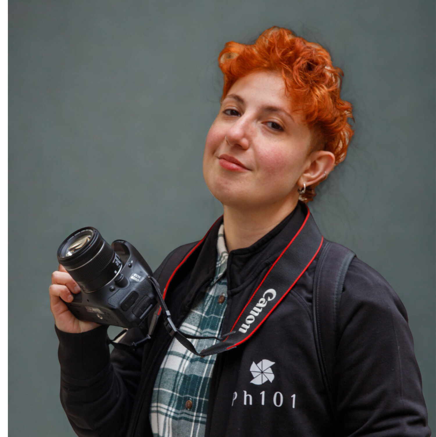 Professional photographer with bright orange hair holding a Canon camera and wearing a plaid shirt.