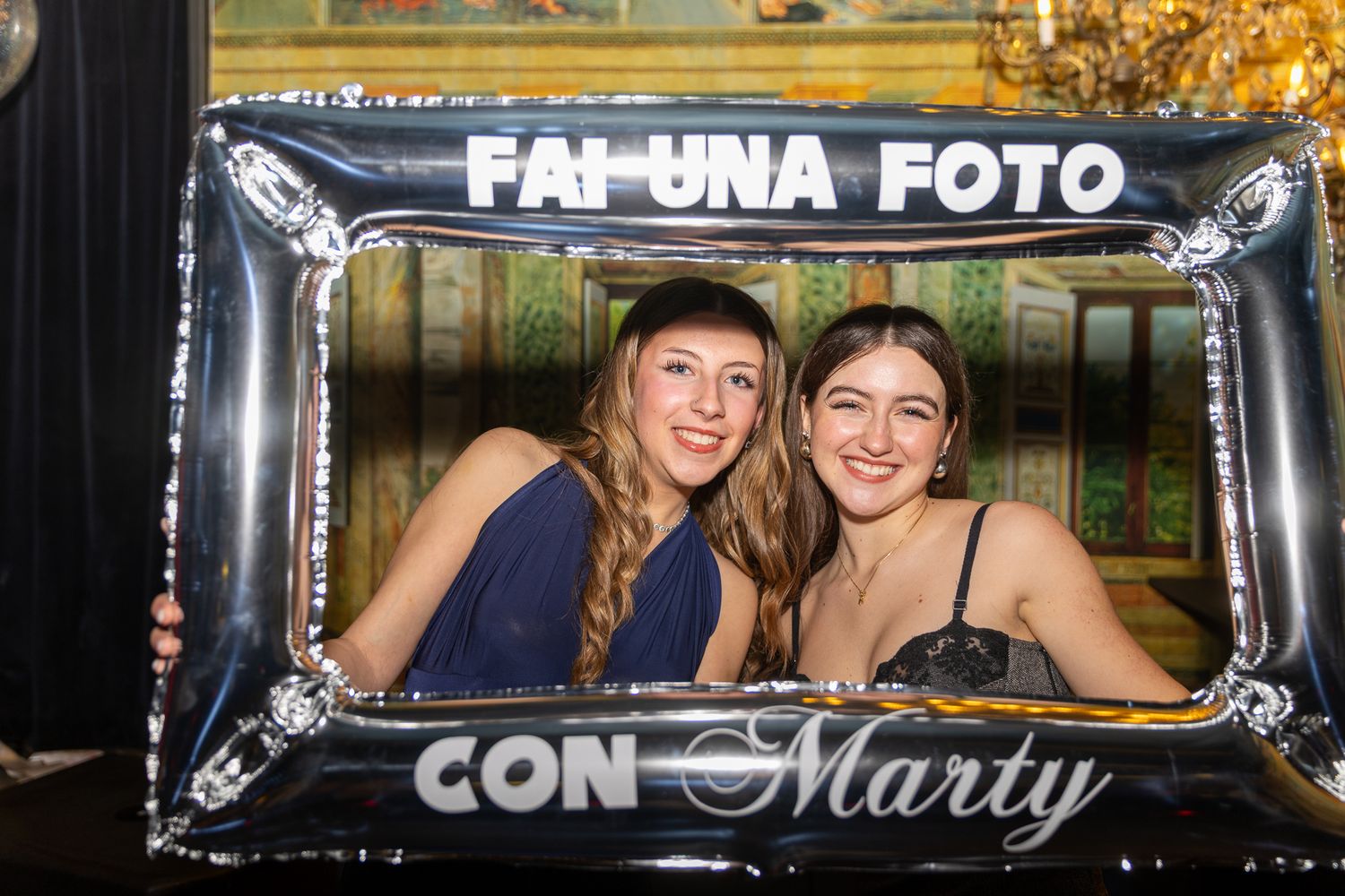 Two people smile while posing with a decorative photo frame that says 'FAI-UNA FOTO CON Marty' at an event.