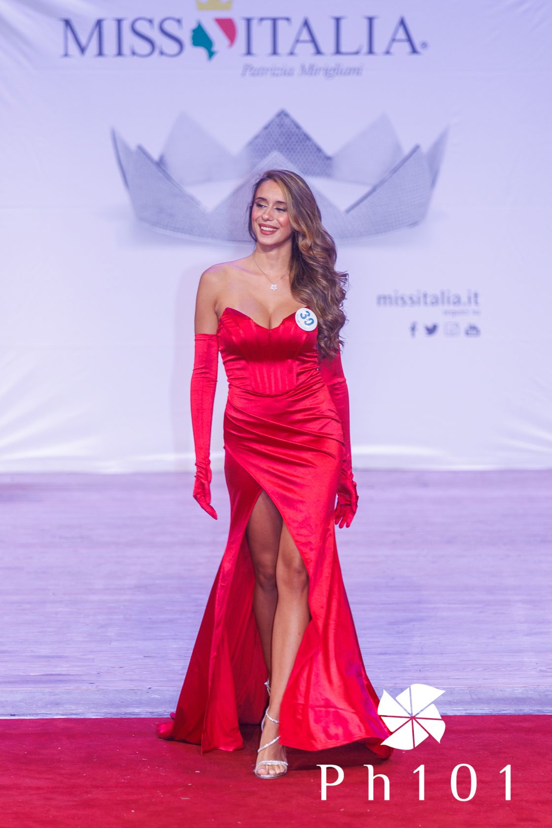 Model in red satin evening gown poses on Miss Italia runway stage.