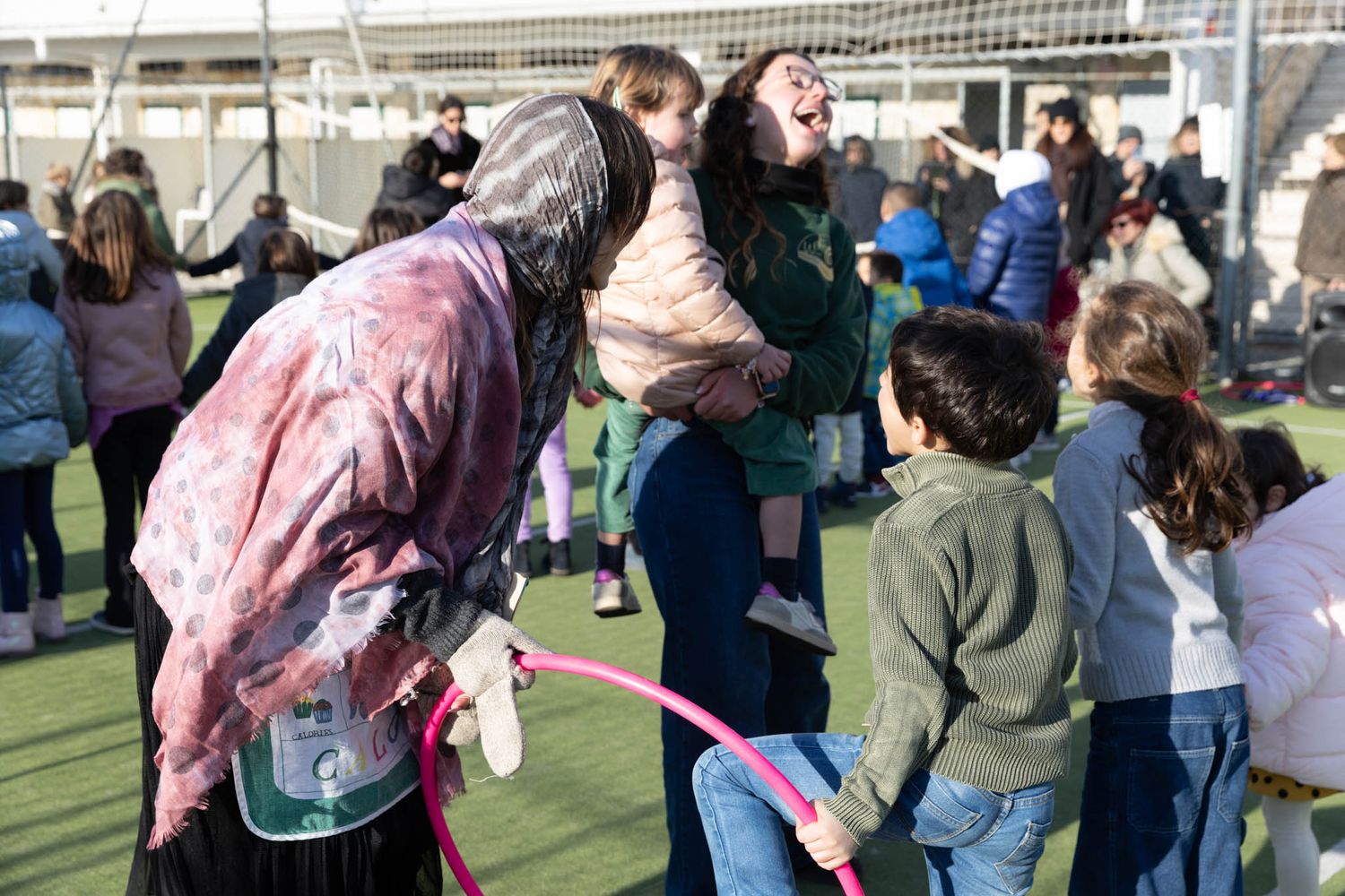 Outdoor sports event with participants and spectators gathered on an artificial turf field.