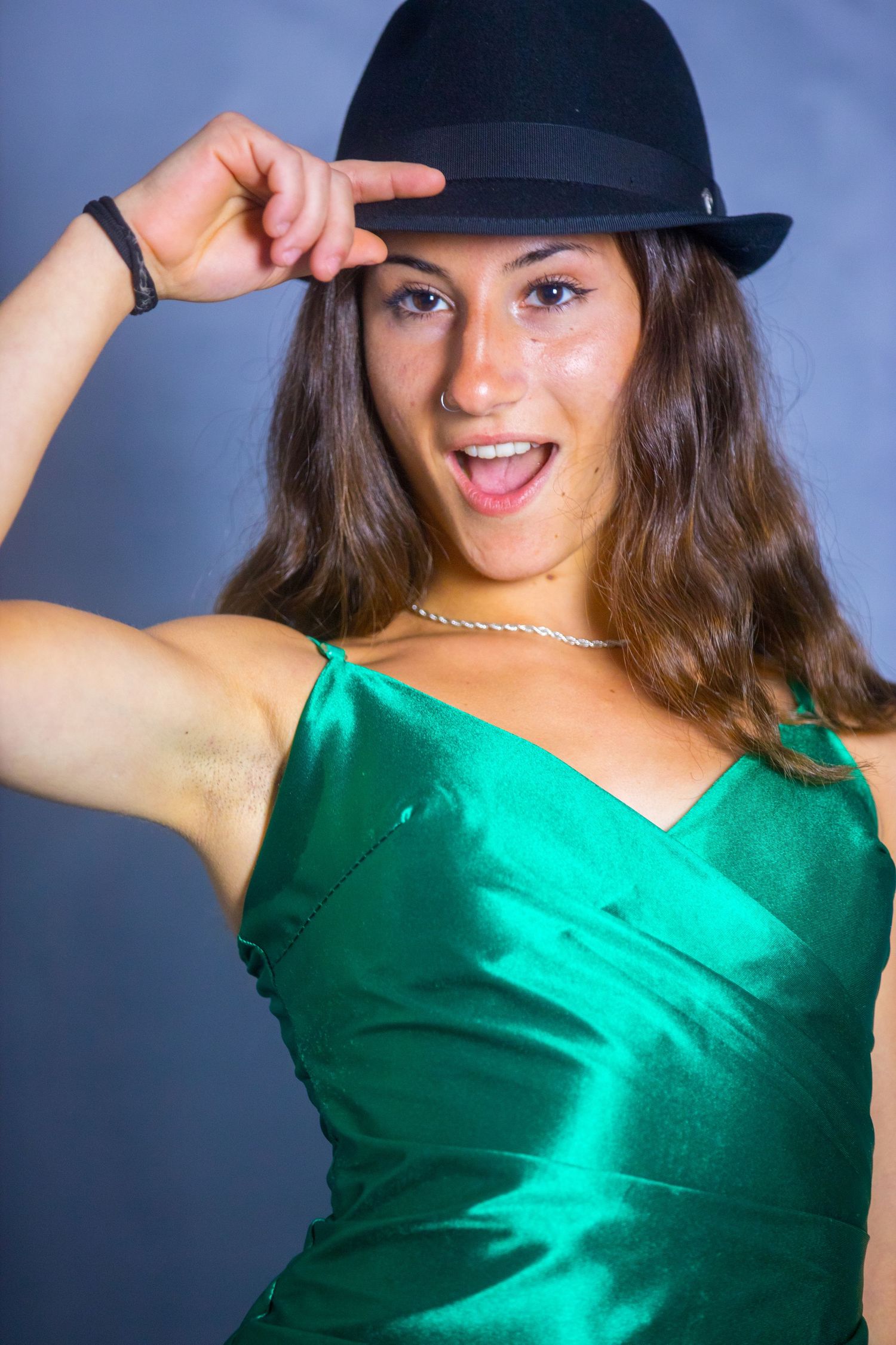 Fashion portraits featuring a bright emerald green satin top and black hat against a blue backdrop.