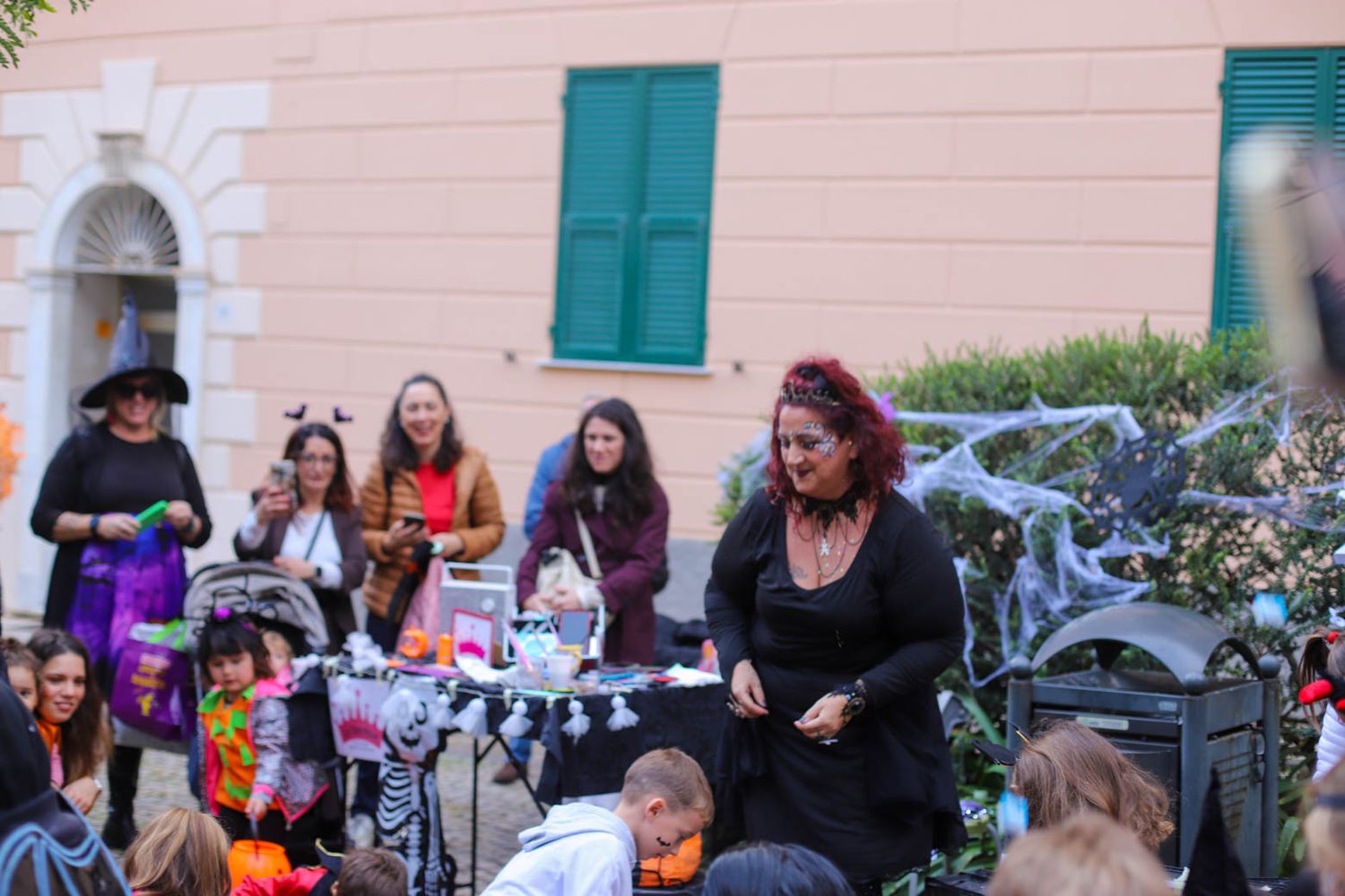 People gathered outside a pink building for a Halloween celebration with decorations.