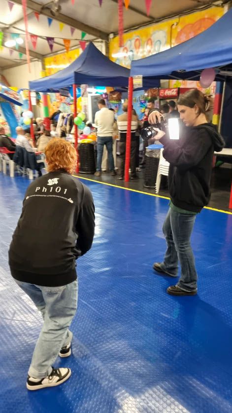 Photographers capturing shots in an indoor venue with blue flooring and colorful banners.