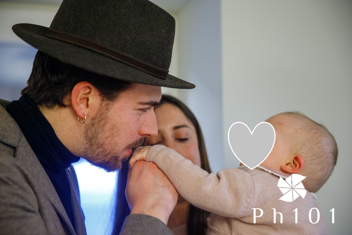 Sweet moment captured as a baby reaches out to touch someone wearing a dark fedora hat.