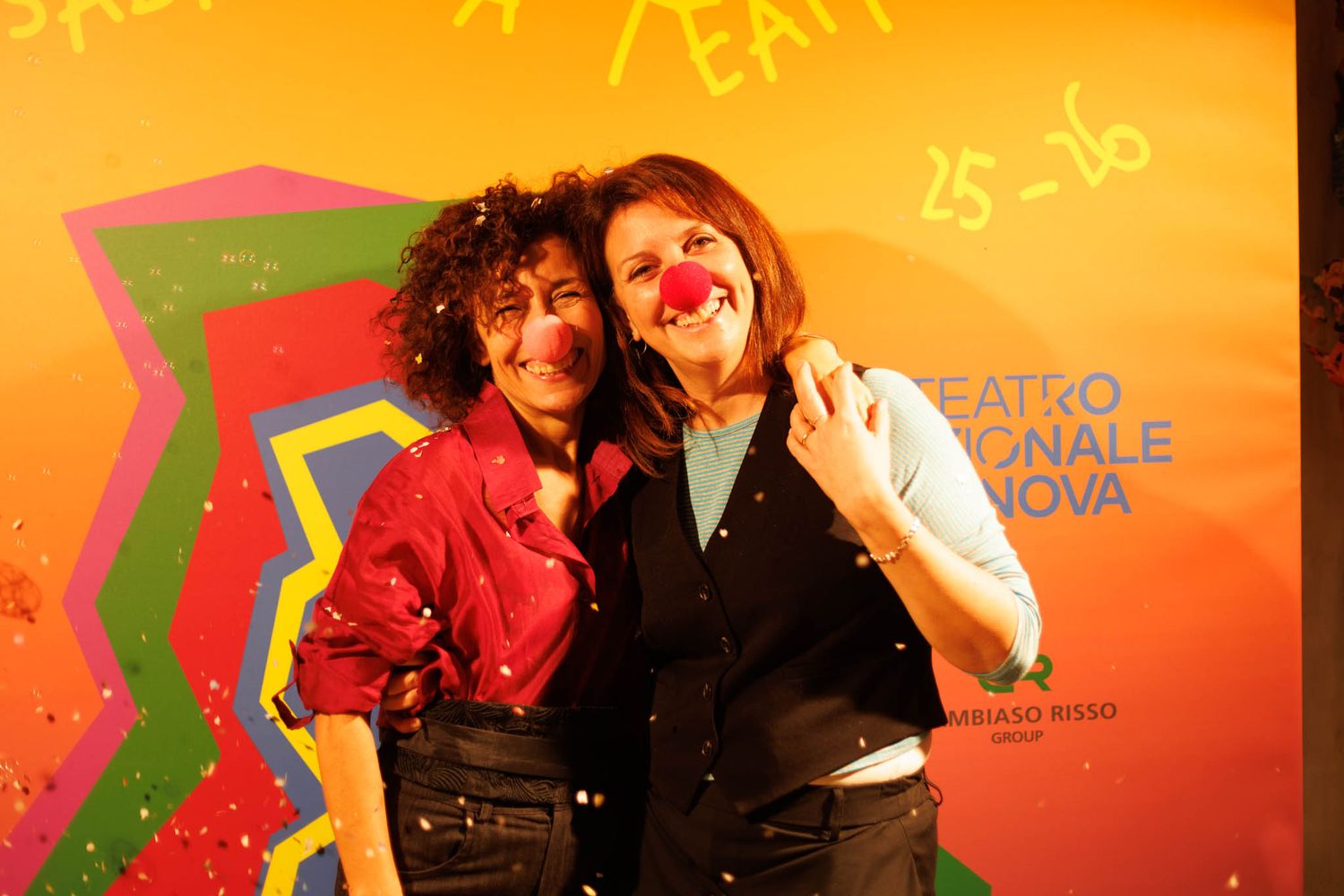 People posing against vibrant orange backdrop with theatrical lighting.