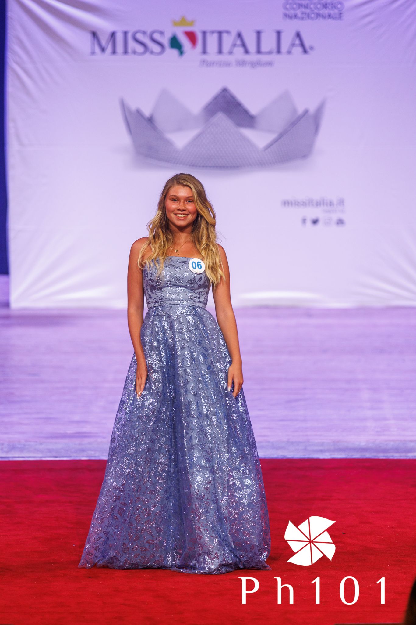 Model wearing sparkly blue ball gown on red carpet at Miss Italia event.