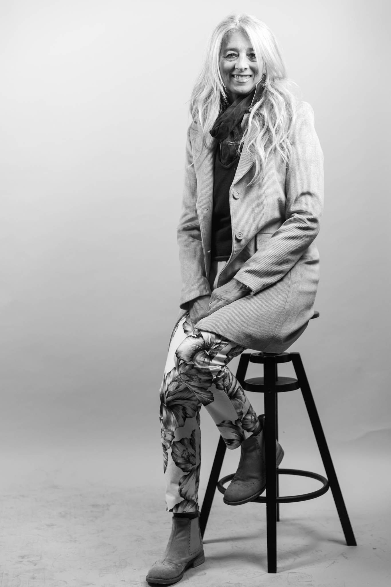 Black and white portrait of woman in coat sitting on stool.
