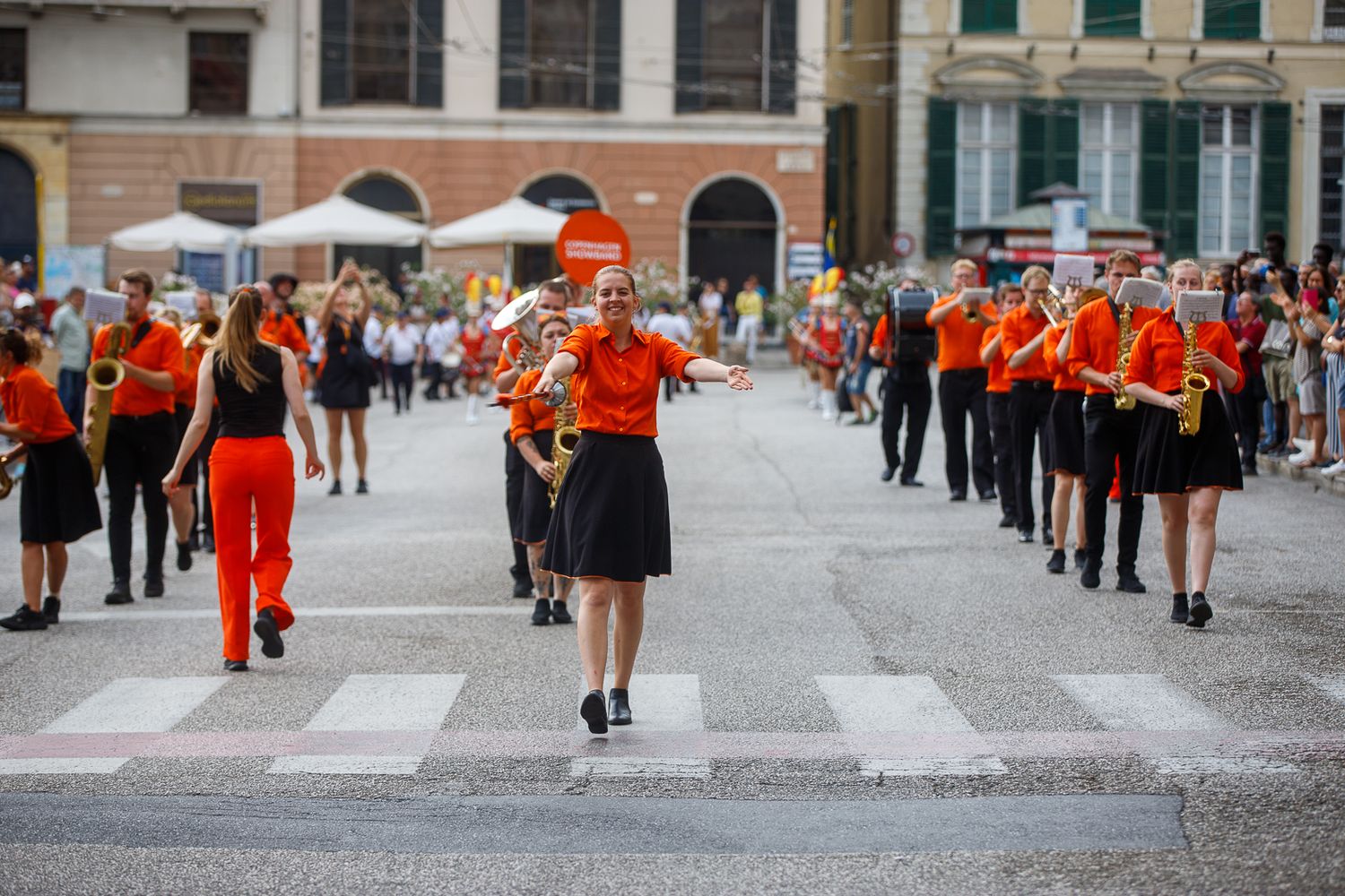 Street performers in bright red outfits dance and entertain crowds in a historic European city square.