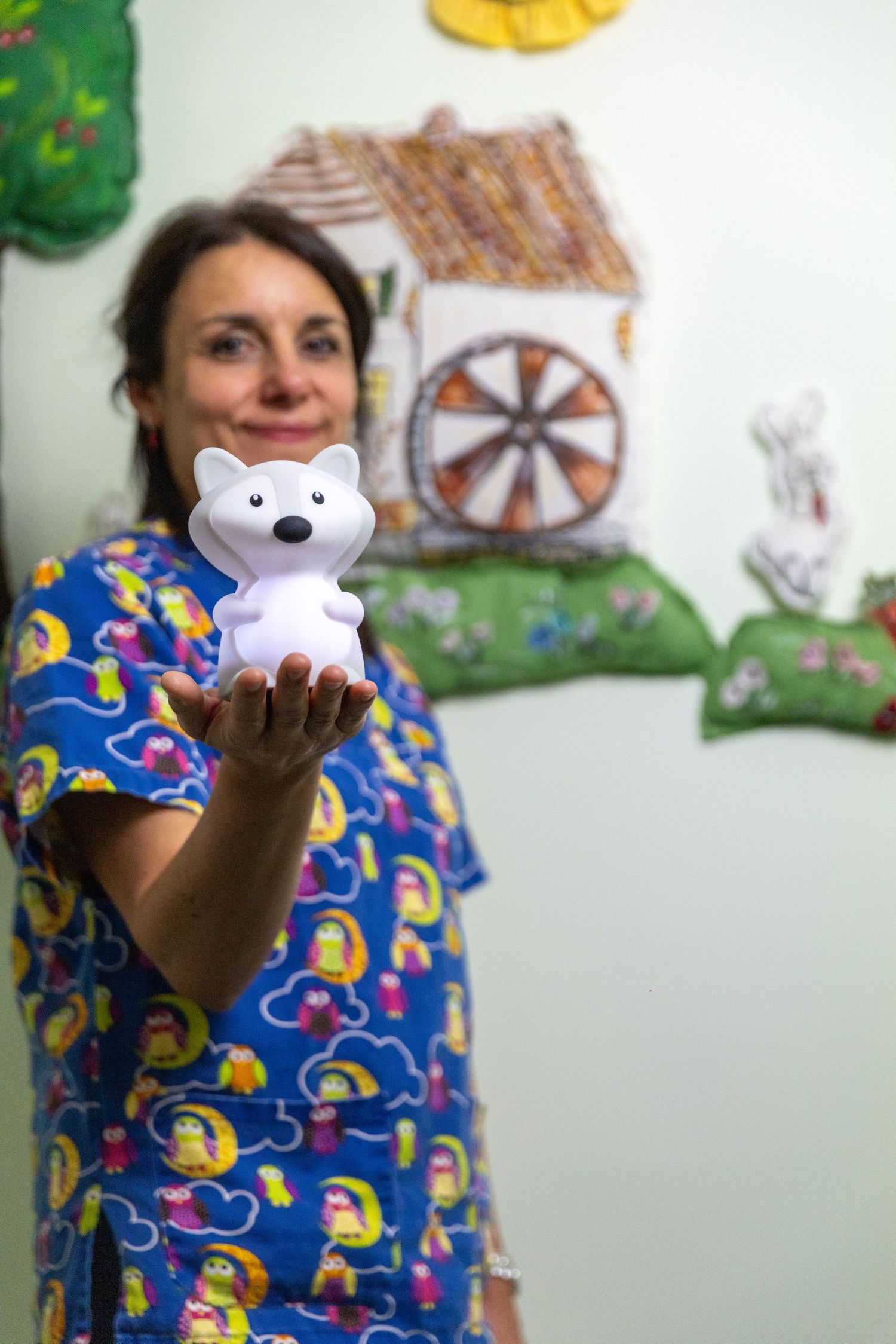 Someone wearing a blue patterned scrub top tosses a small white teddy bear decoration in the air.