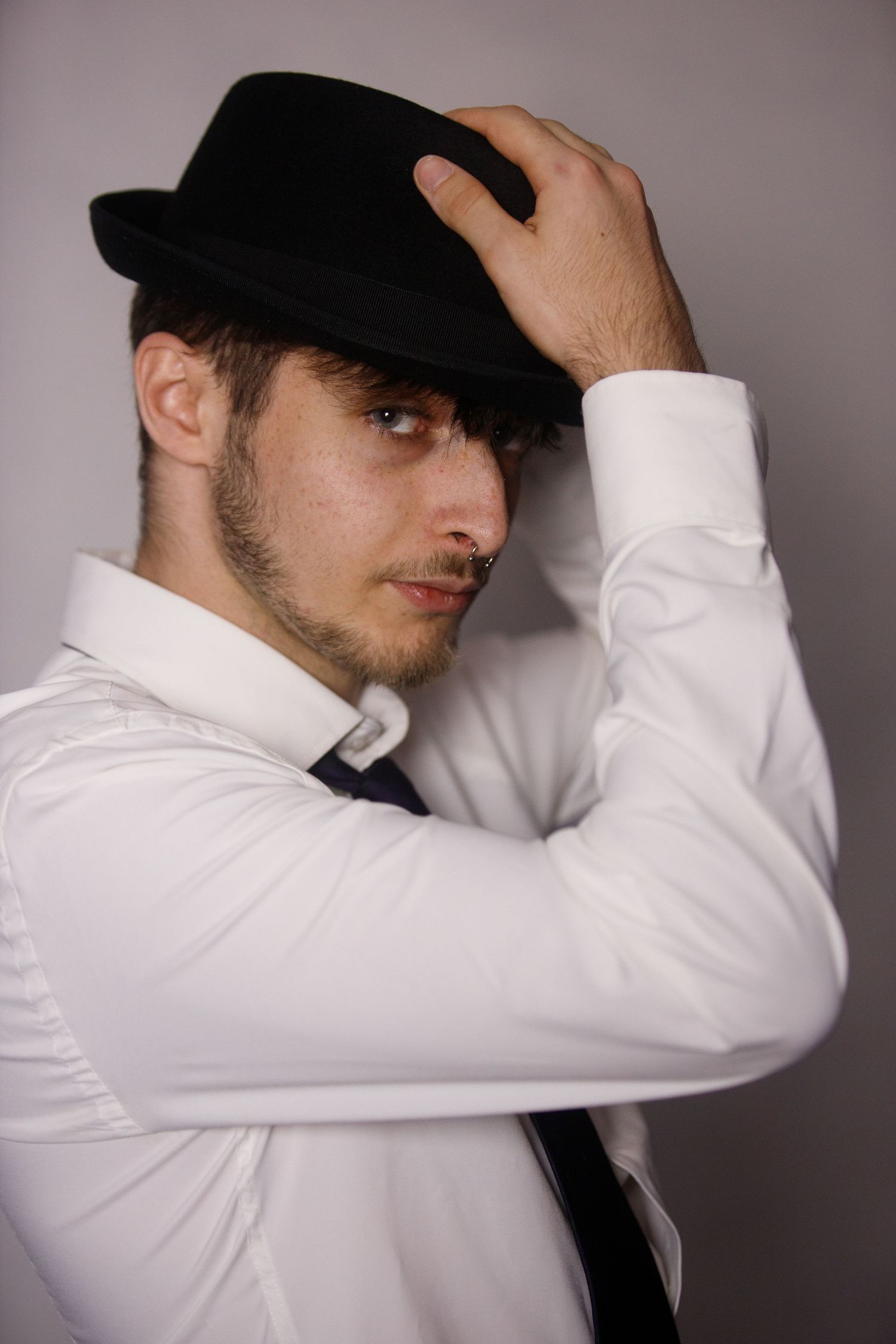 Artistic portrait series showing someone in a white shirt and black hat making dramatic gestures against a gray background.