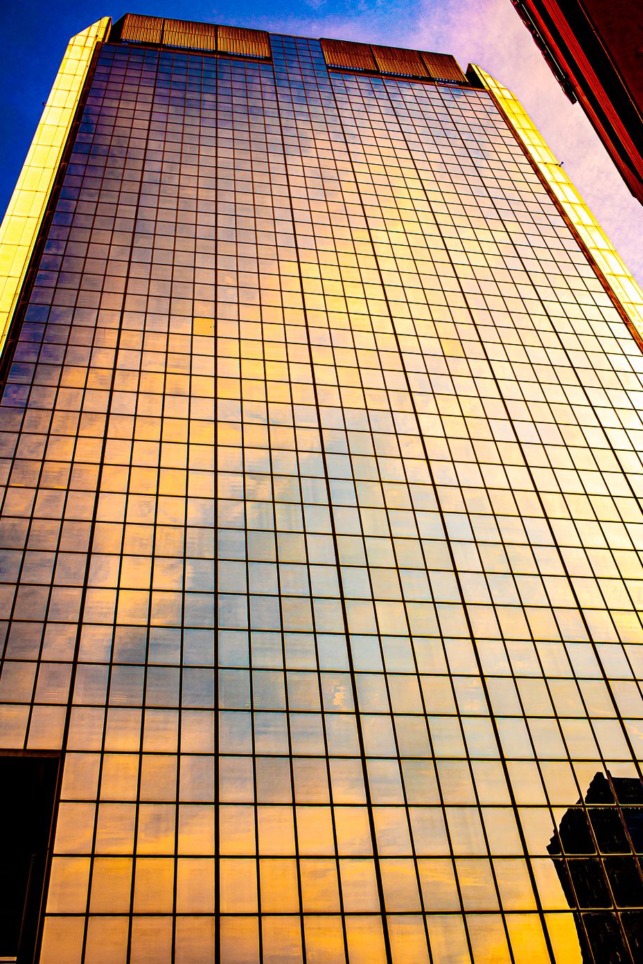 Glass office building facade reflecting golden sunset light in a grid pattern.