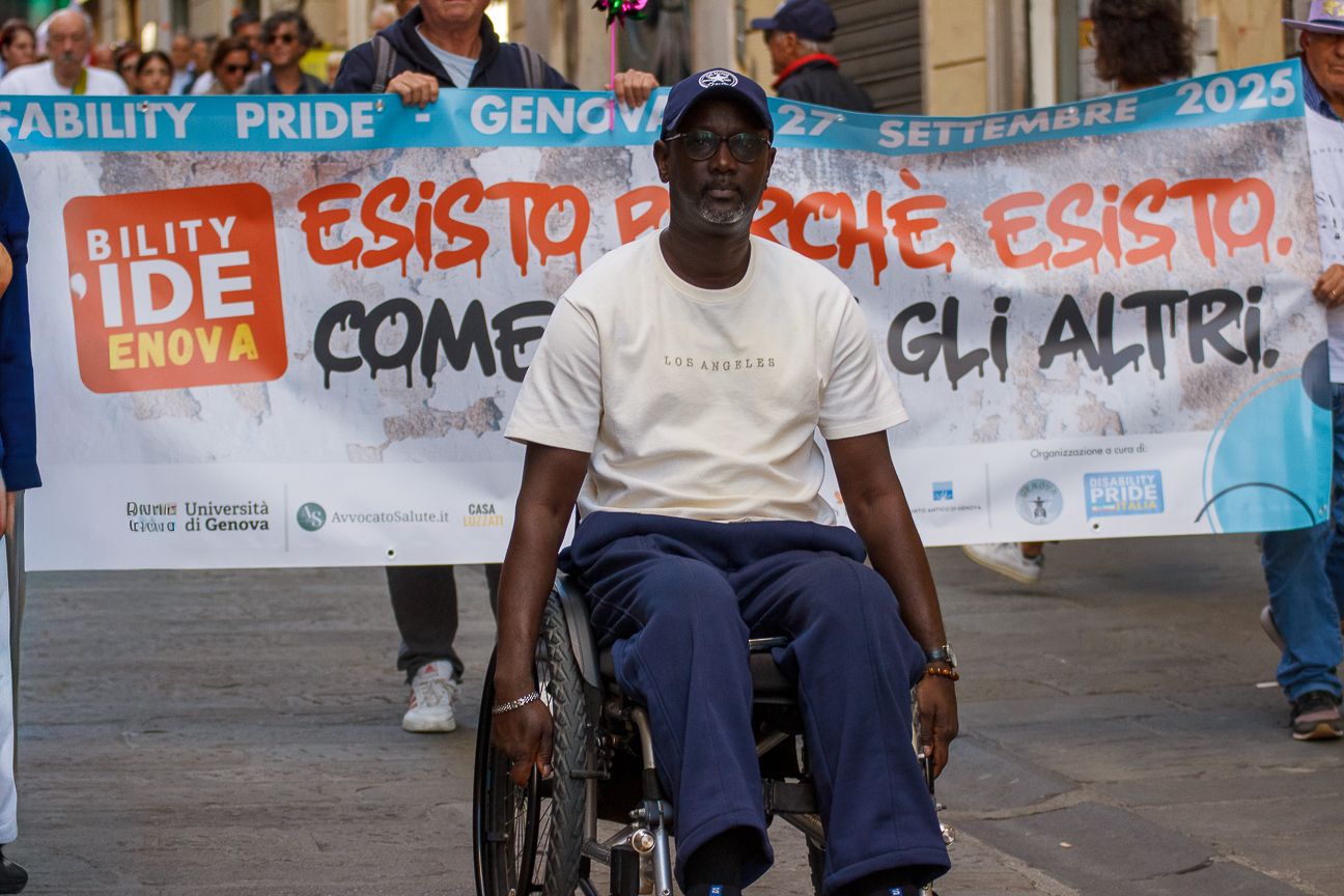 Person in wheelchair participates in disability pride demonstration with banner behind.