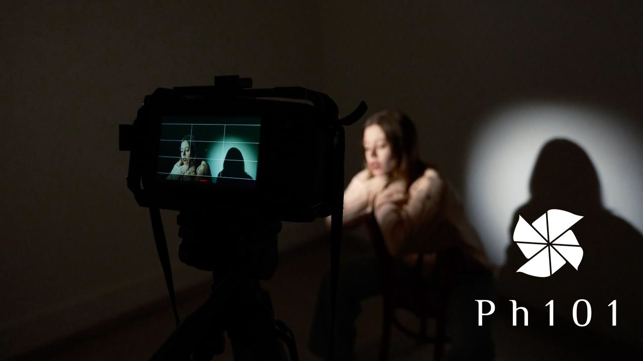 A dark silhouette of a person holding a camera against a bright background with lens flare effects.