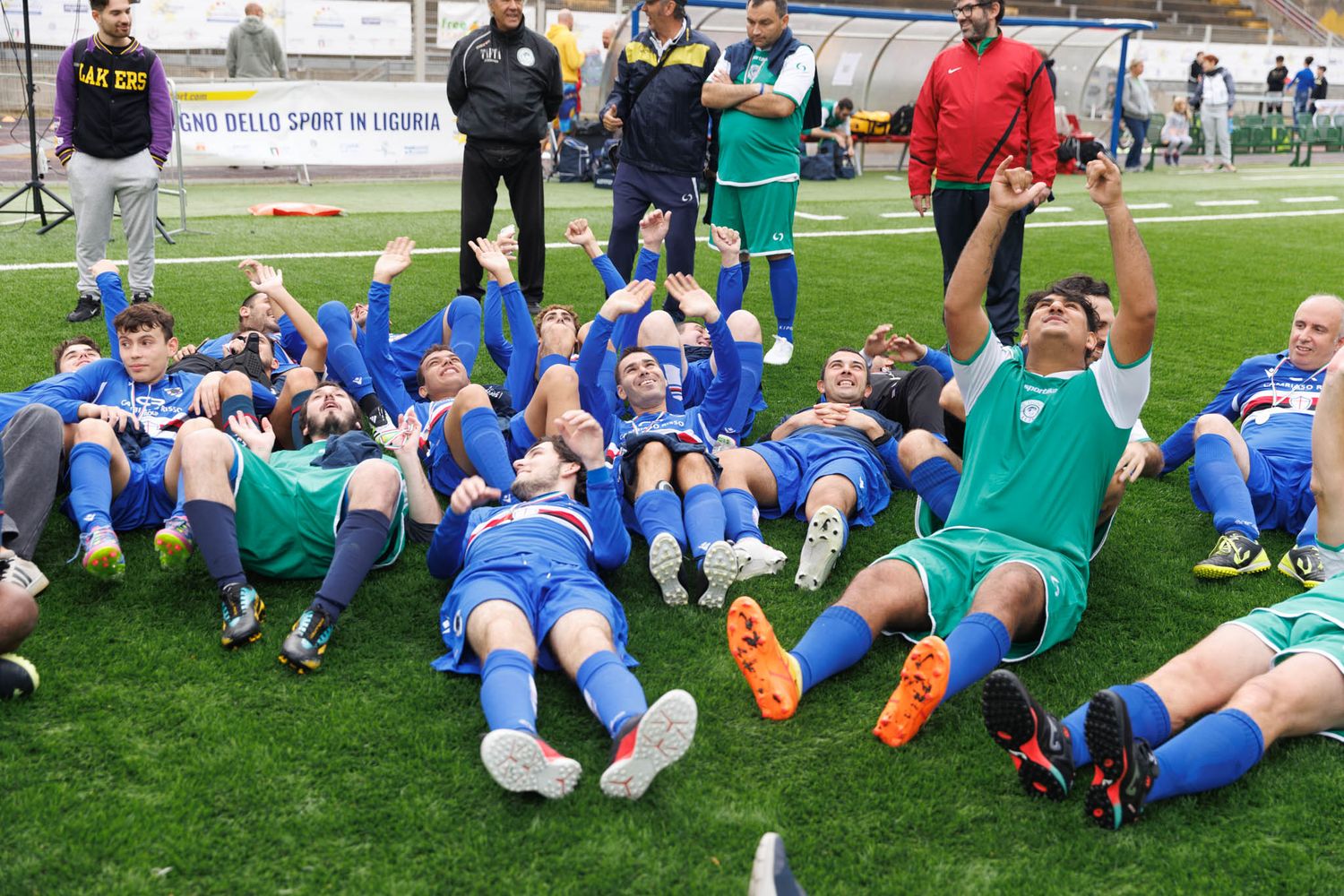 Athletes in blue and green uniforms doing stretching exercises on a grass field.
