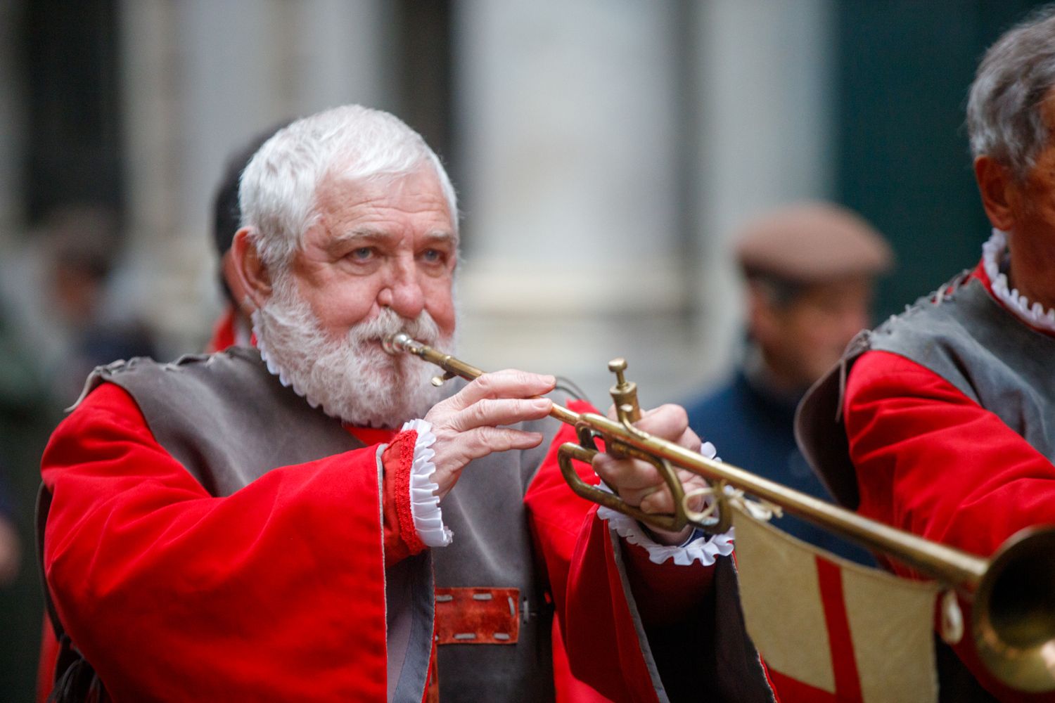 Musicians in red uniforms perform with brass instruments during a ceremonial event.