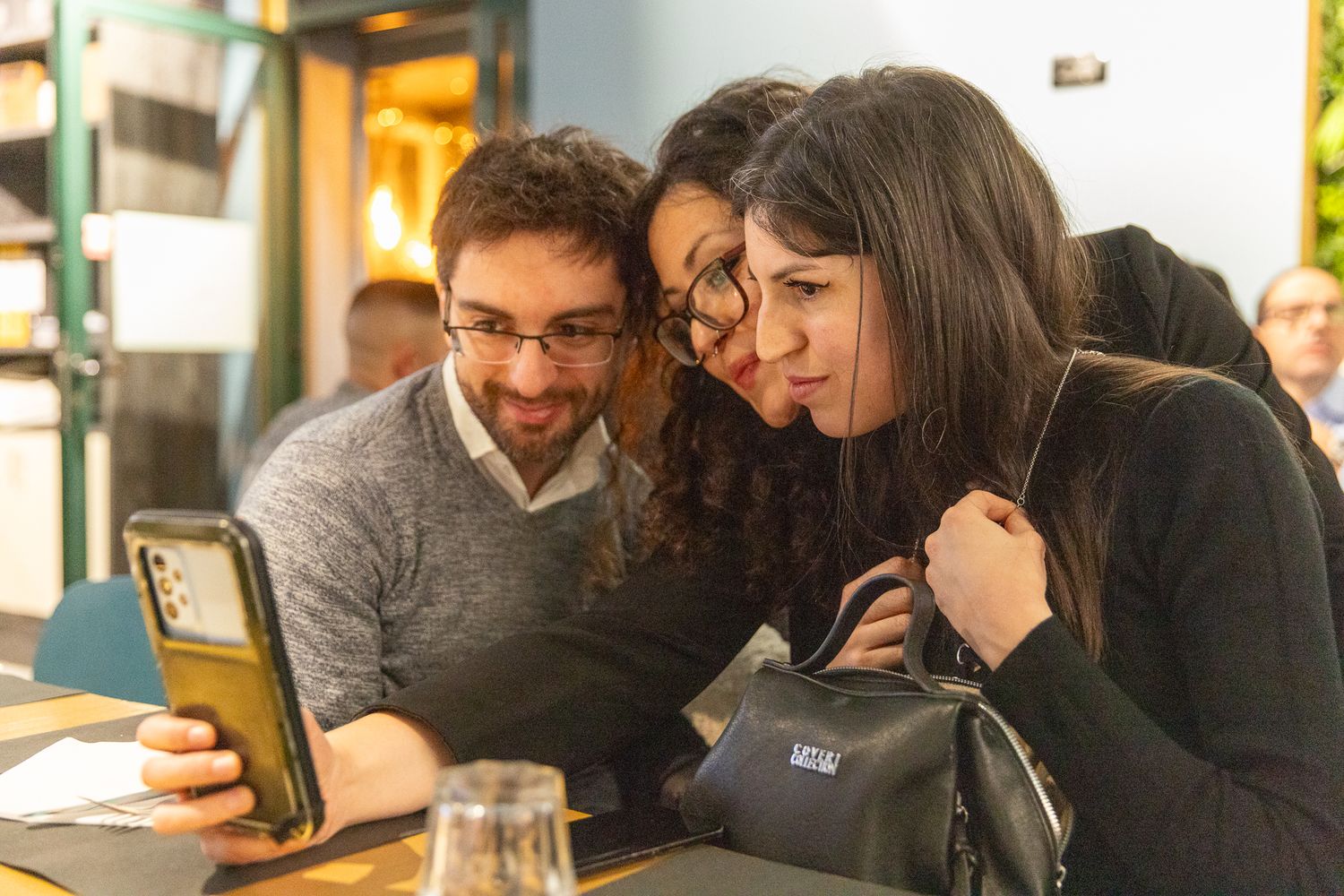 A group of people sit together at tables in a restaurant or cafe having conversations and sharing drinks.