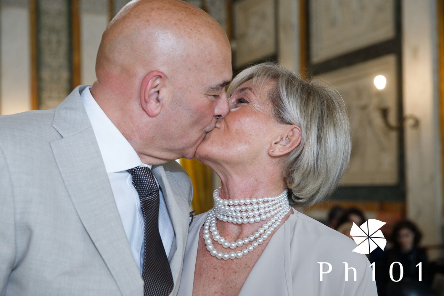 Elegant couple sharing a romantic kiss at a formal event, with the woman wearing a pearl necklace.