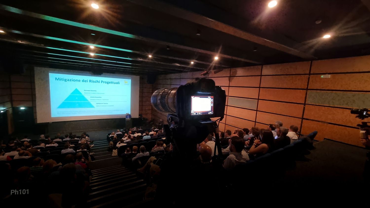 Wide angle shot of a lecture hall with illuminated ceiling and presentation screen.