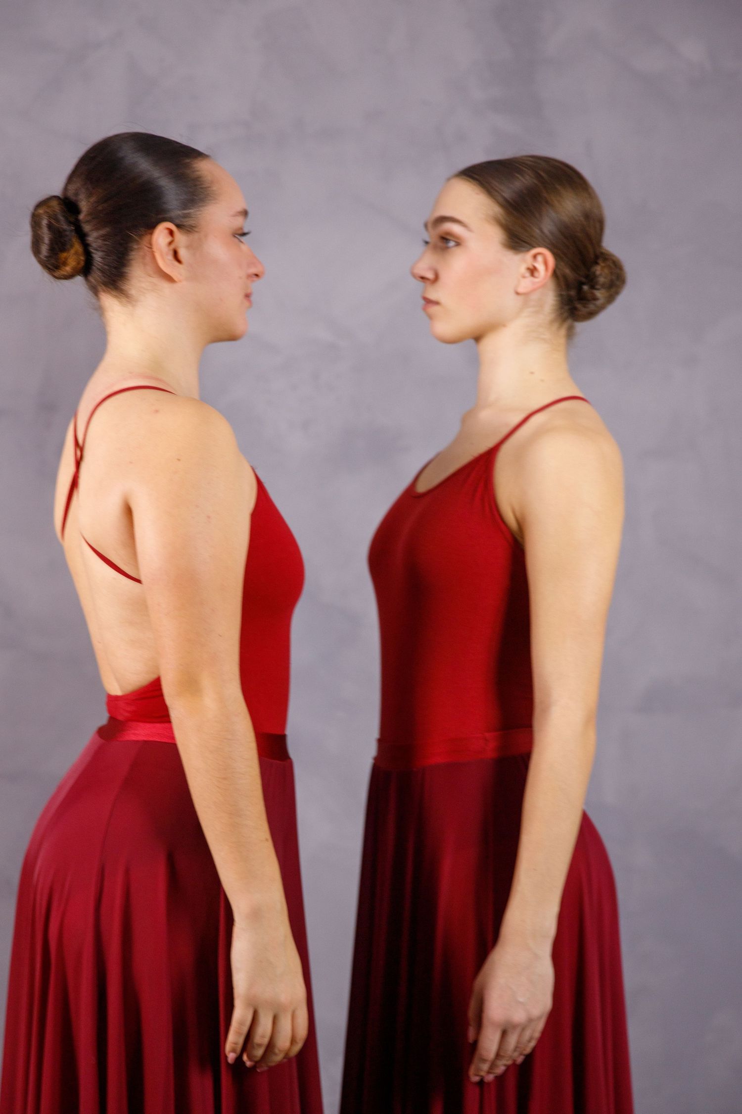 Two dancers in burgundy dresses standing face to face in dramatic pose.
