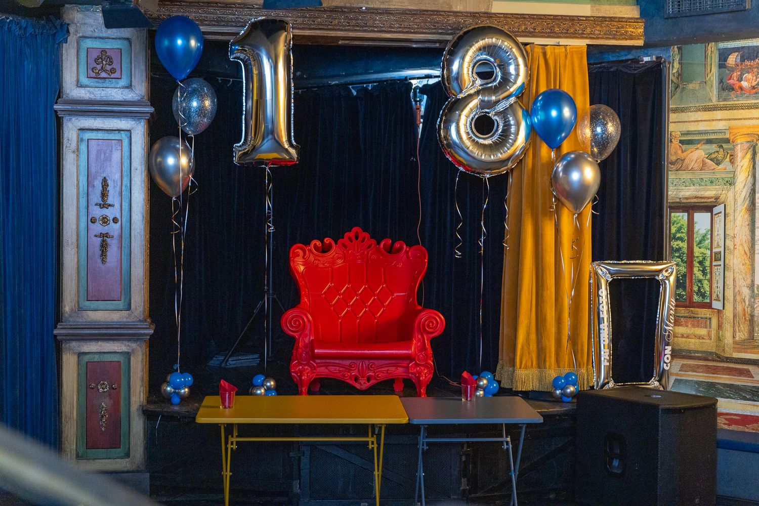Ornate vintage theater interior with red velvet seating, gold trim details, and crystal chandeliers illuminating the space.