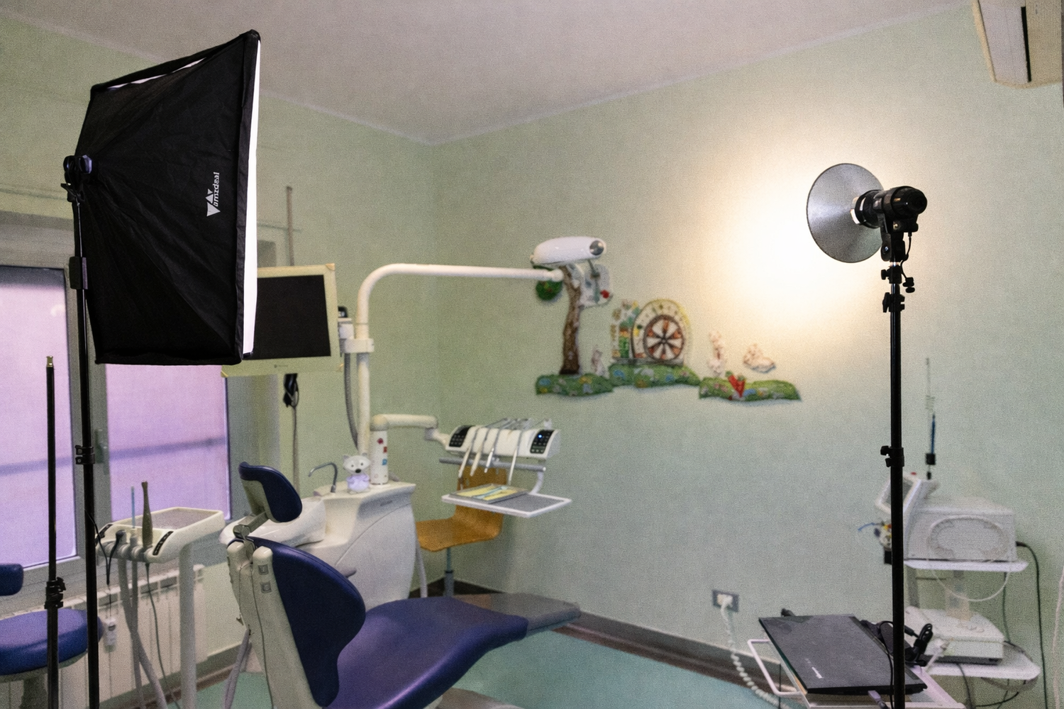 Modern dental examination room with blue chair, overhead lights, and medical equipment mounted on white walls.