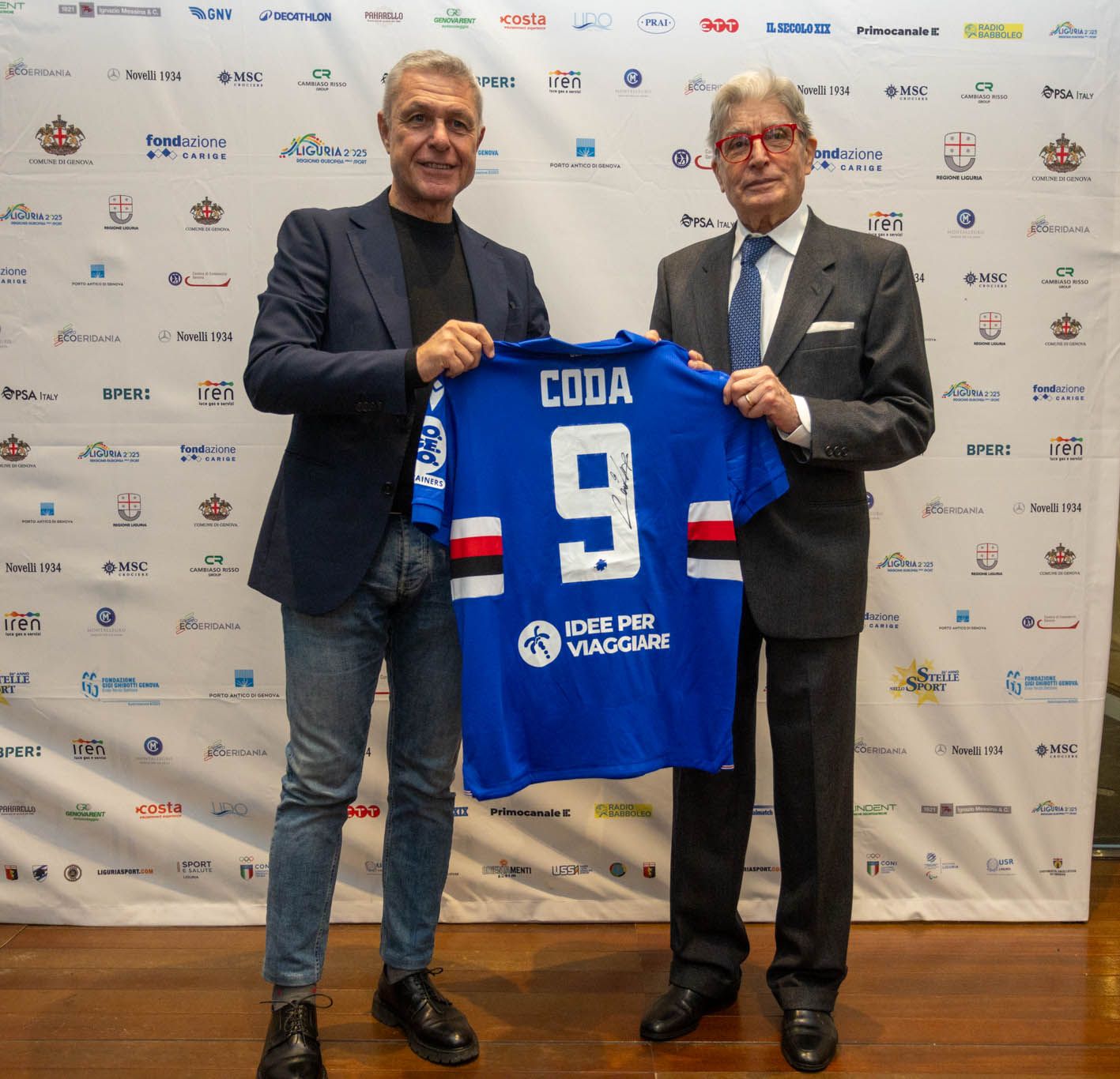 Two men holding up blue sports jerseys at sponsorship or presentation event.
