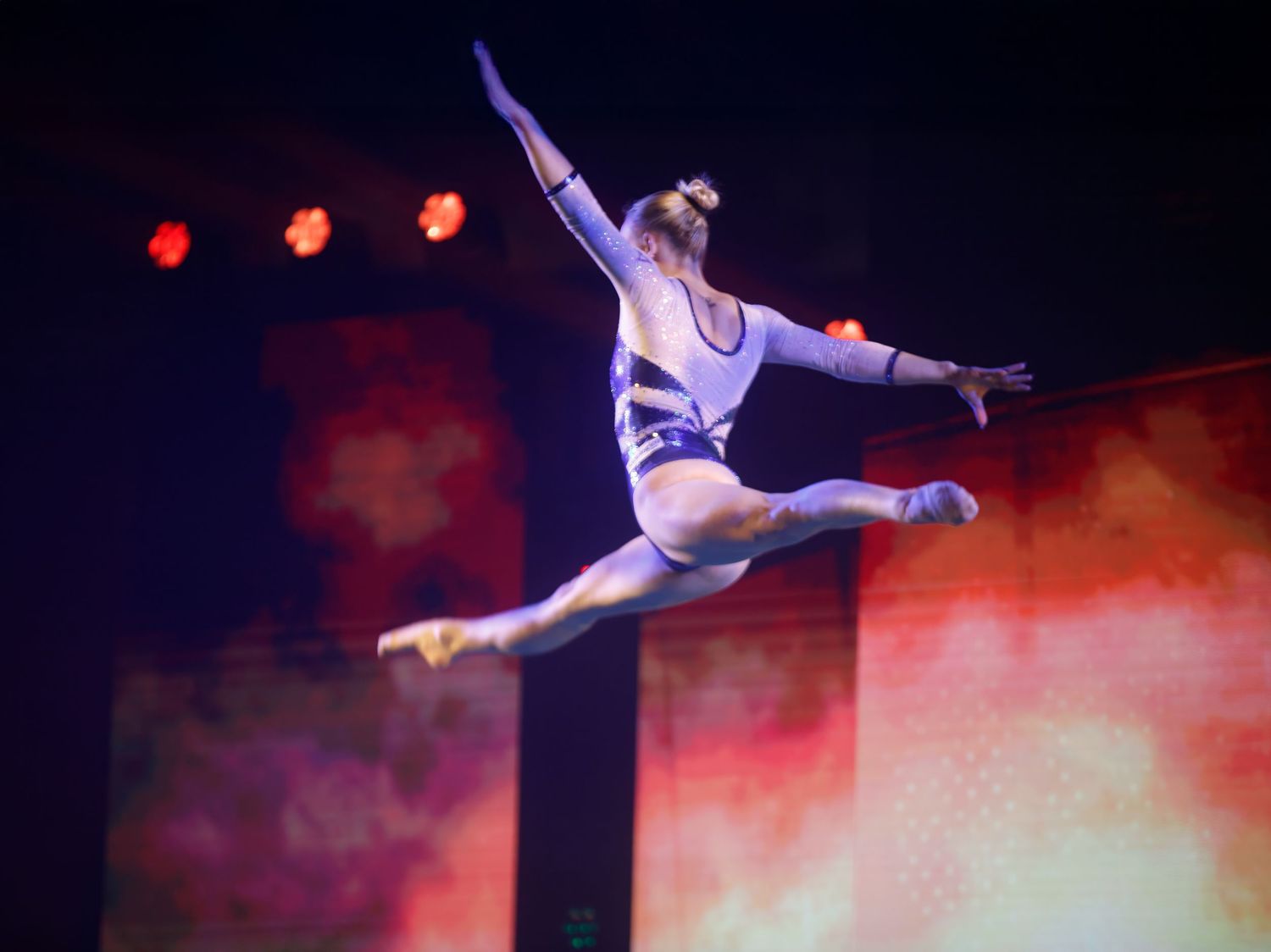 Acrobatic performers in white costumes performing aerial stunts against dramatic lighting.