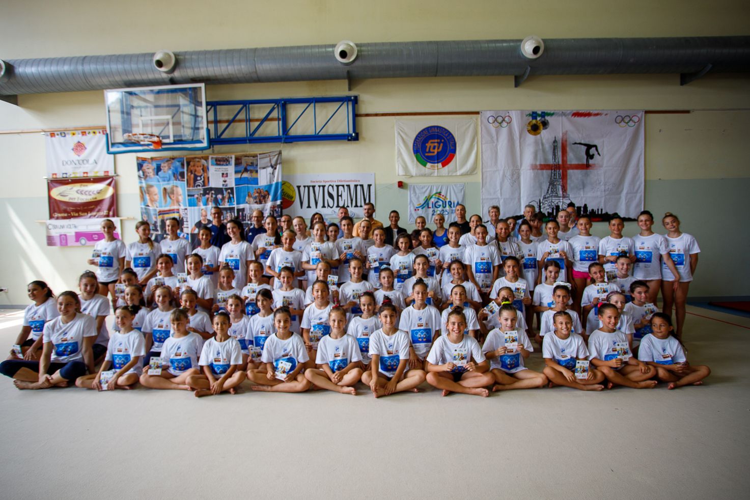 Large panoramic group photo of students in matching uniforms seated in gymnasium.