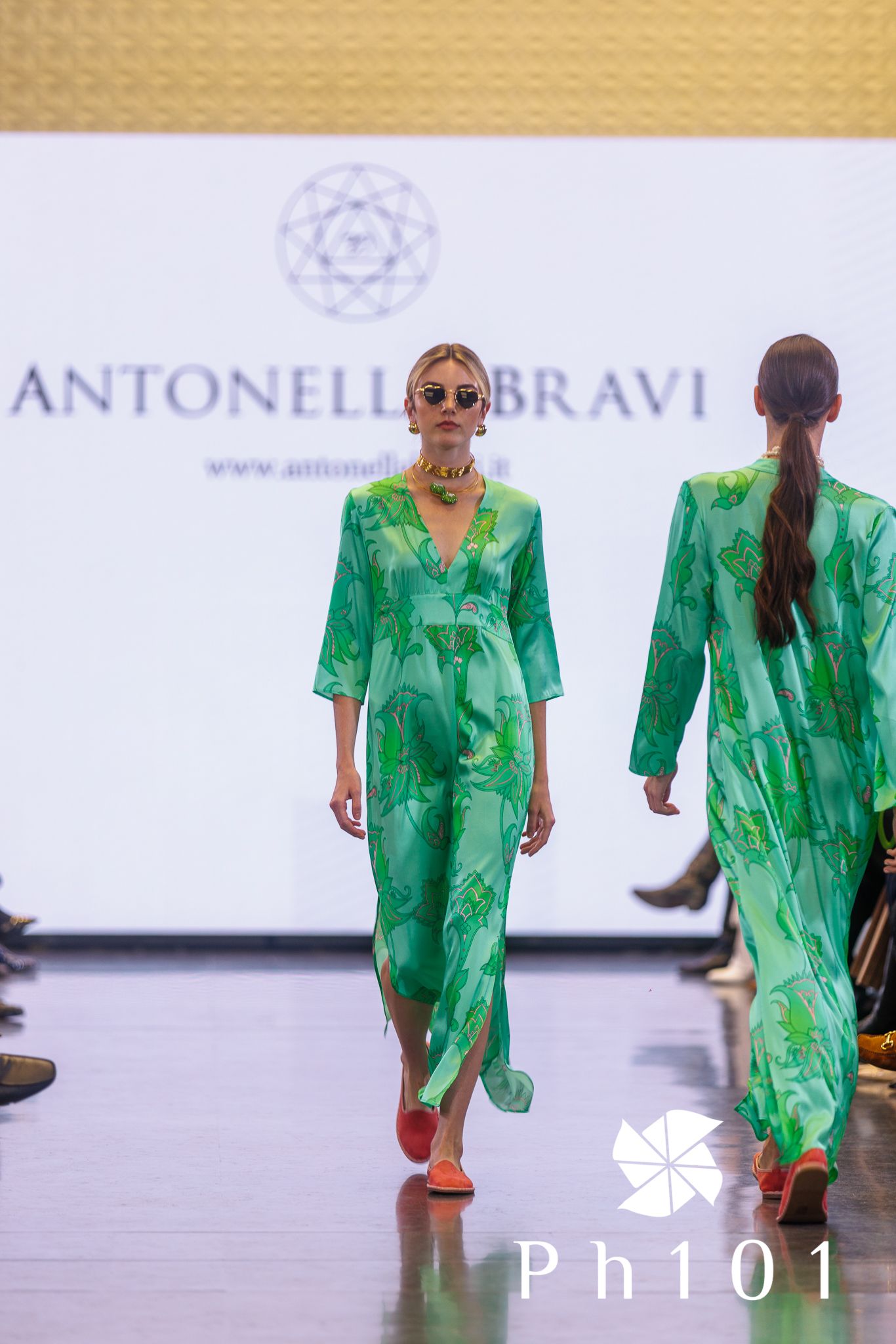 Models showcase vibrant green designer outfits on runway at Antonella Bravi fashion show.