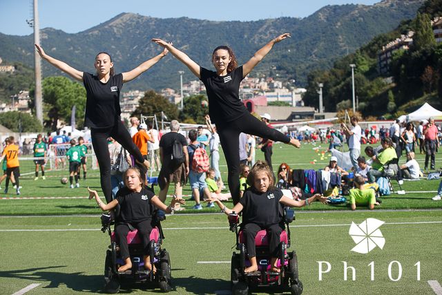 Wheelchair athletes celebrating with arms raised on an outdoor sports field with mountains in background.
