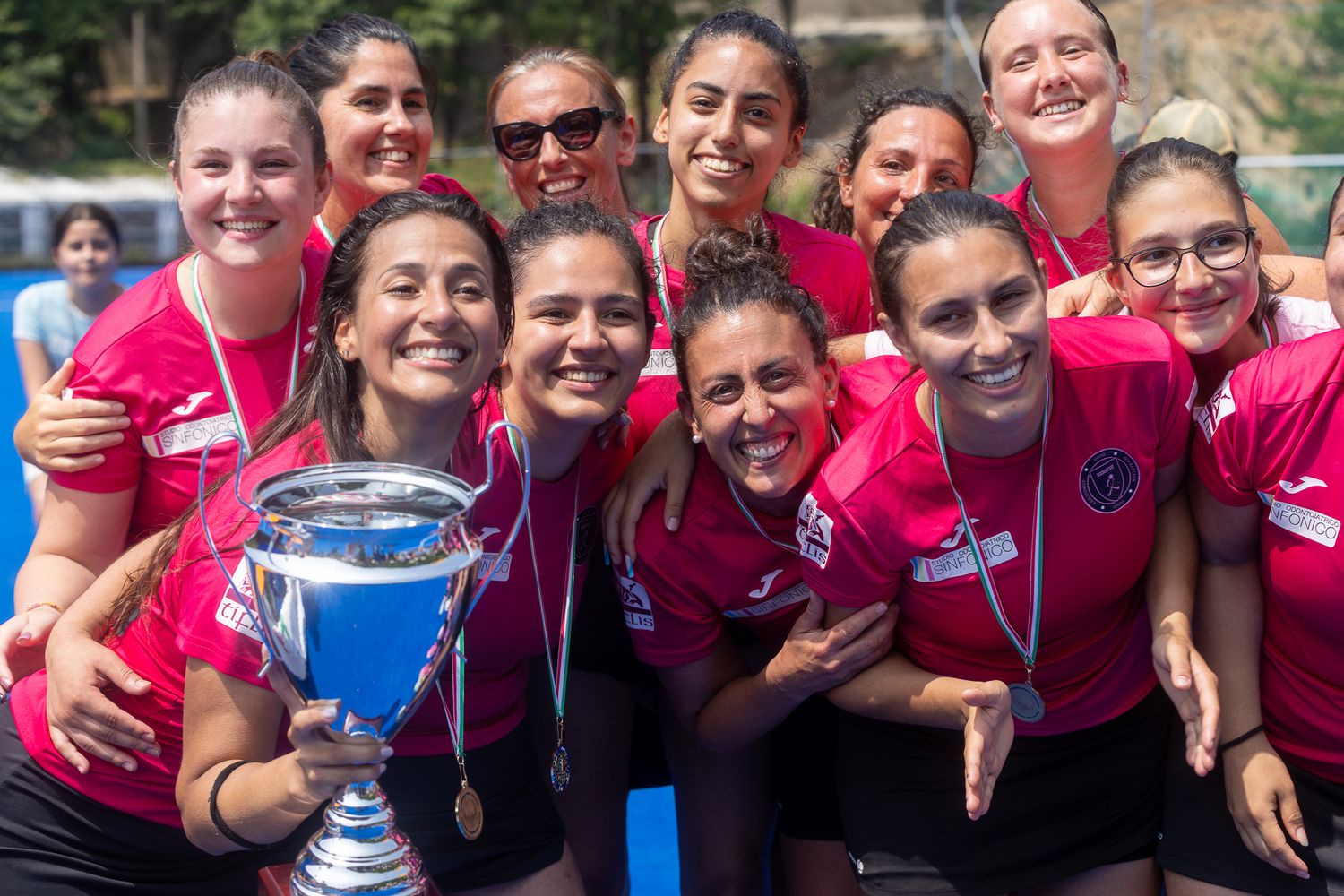 Team members in pink uniforms celebrate together on a sports field.