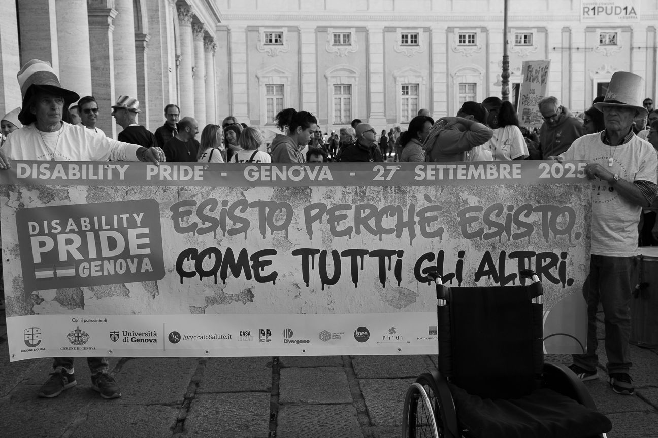 Protesters hold a disability pride banner with Italian text at a public demonstration.