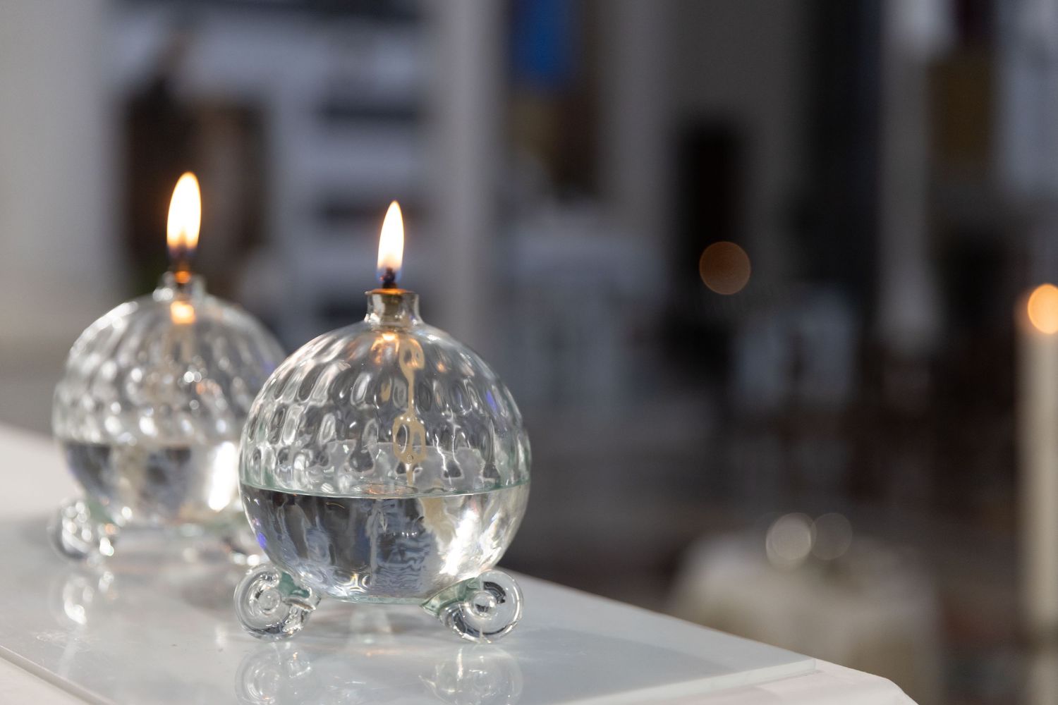 Row of lit glass oil candles creating ambient lighting on white surface.