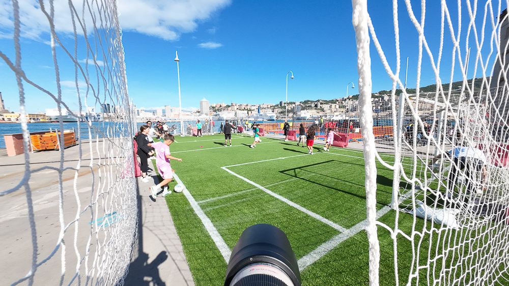 Soccer field view through goal net with players visible in the distance.