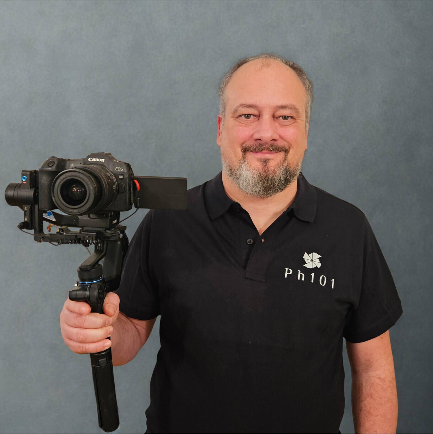 Professional videographer holding a stabilized camera rig while wearing a branded polo shirt.