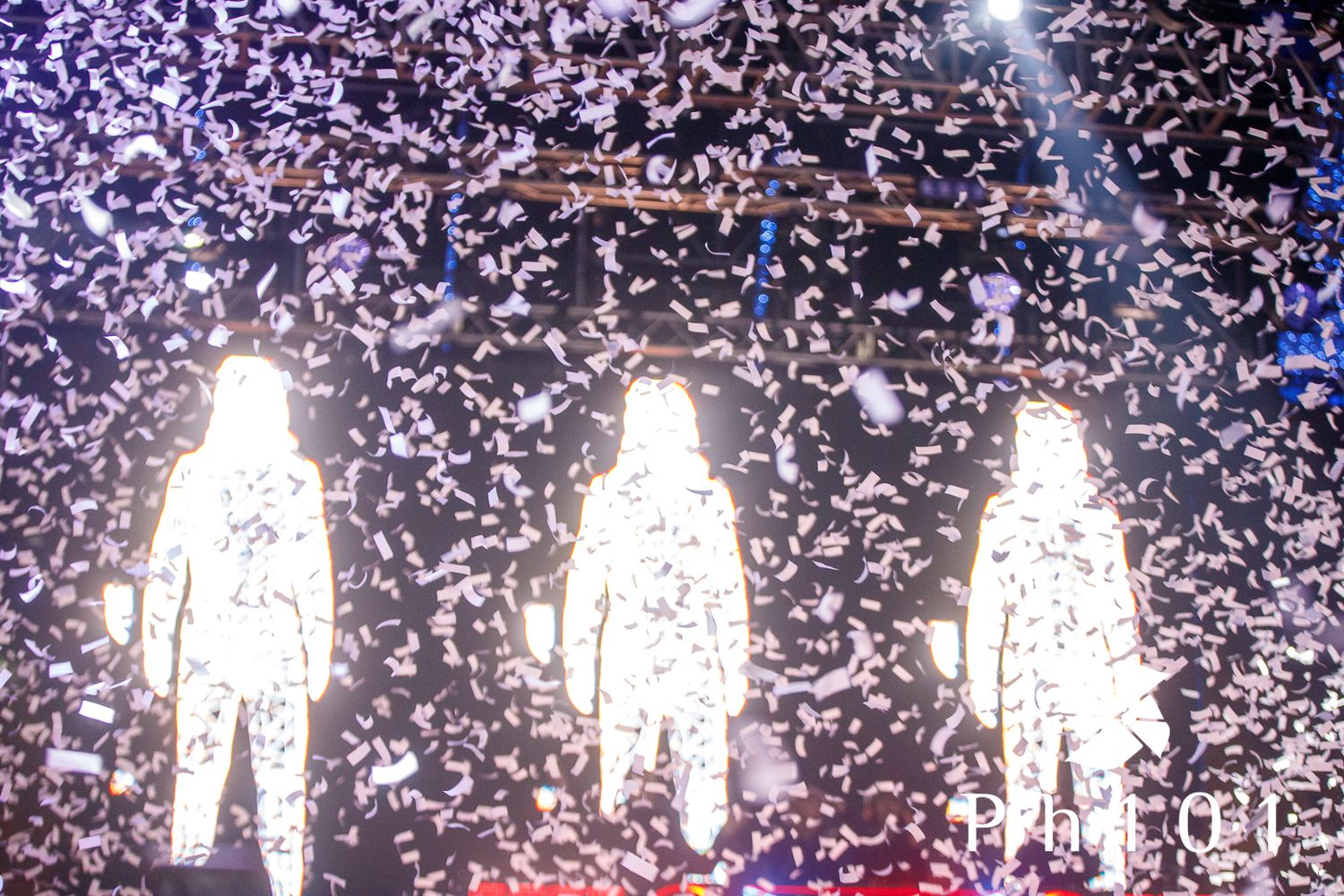 White silhouettes of people with confetti falling in concert venue.