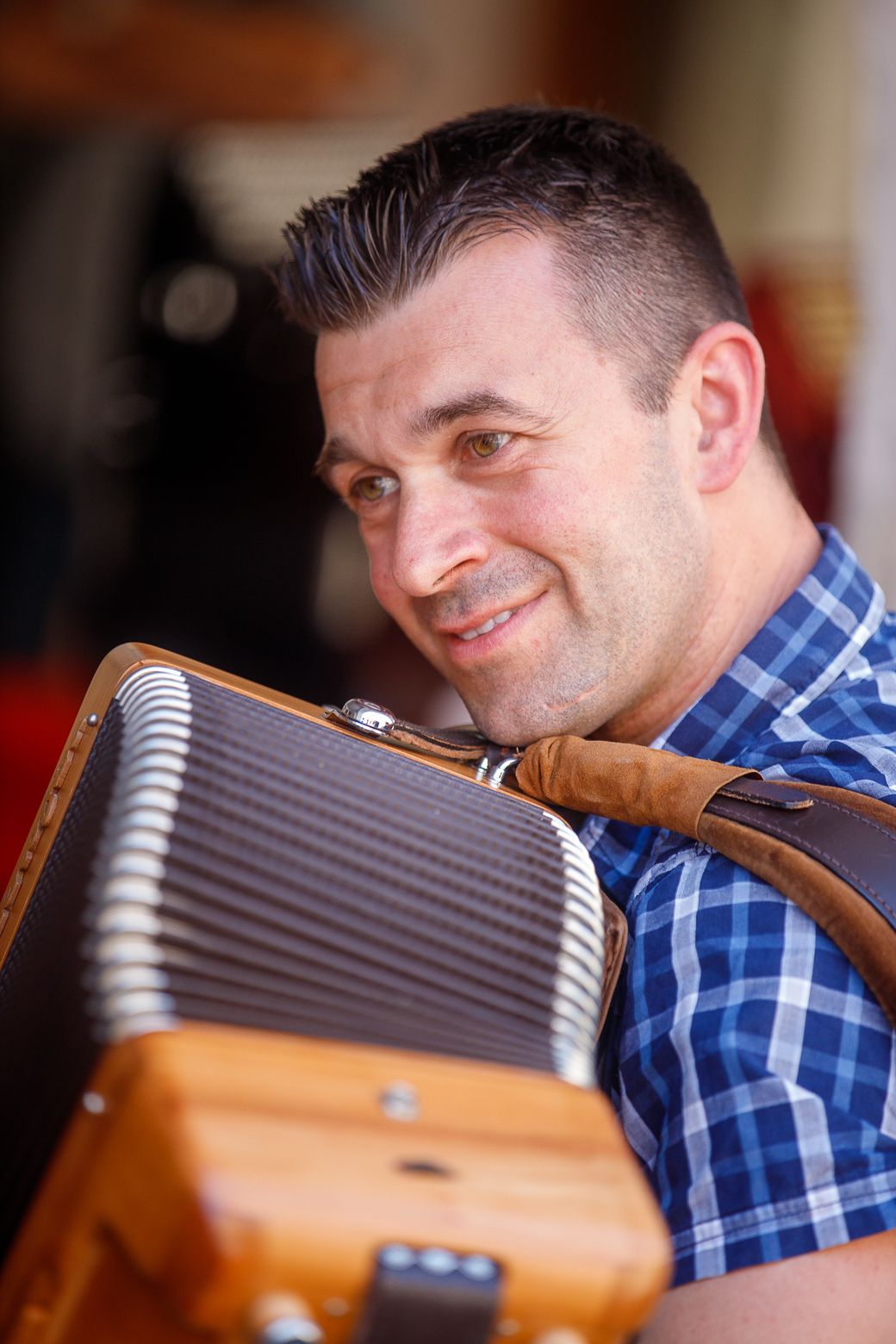 Person in blue plaid shirt examining an acoustic guitar neck in studio lighting.