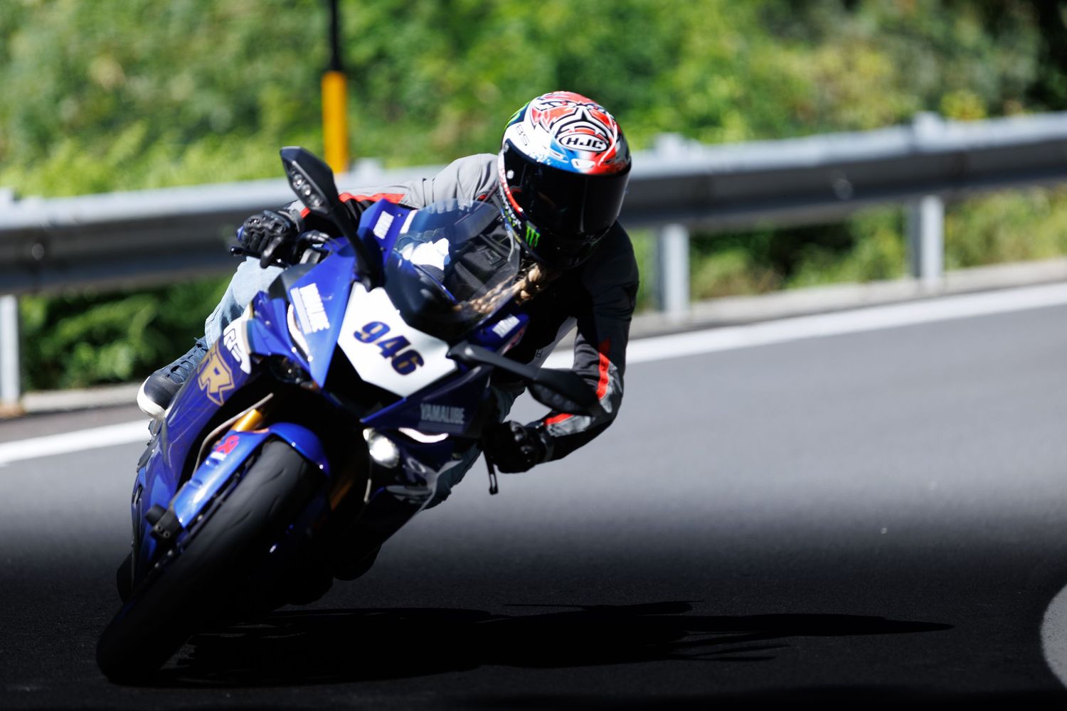 Blue racing motorcycle speeds around a curve on a winding mountain road.
